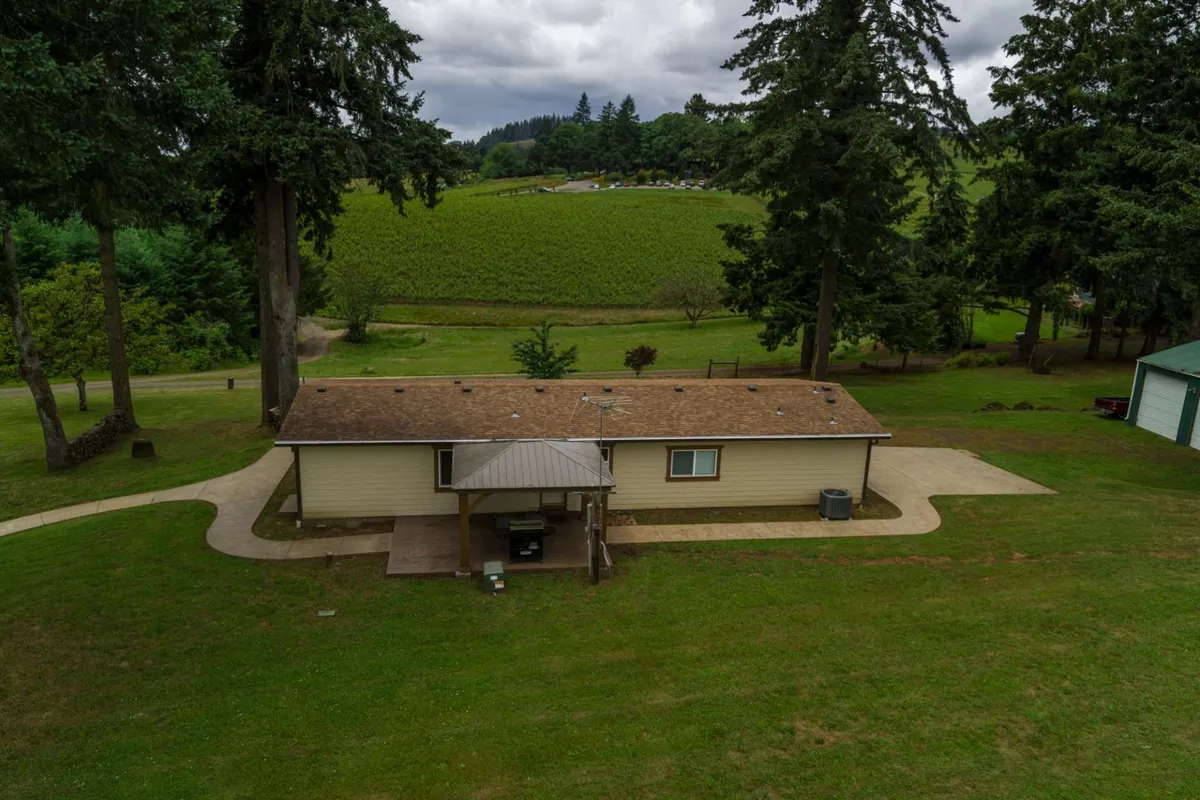 An exterior shot of the house, surrounded by lush landscape with a clear pathway leading up. The porch is visible, suggesting further outdoor gathering spaces, and the scene is set during golden hour, emphasizing the tranquil, welcoming mood of the property and its connection to the surrounding vineyards.