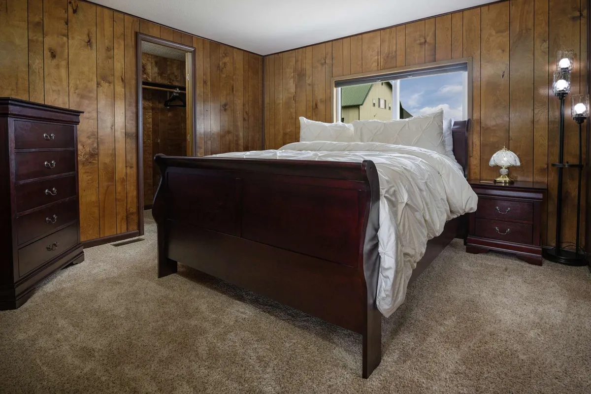 A calming bedroom scene with a queen-size bed, warm wooden furniture, and a window overlooking the outdoors. The soft light and cozy setting make it ideal for quiet evenings or restful mornings, aligning with the idea of a private retreat for guests.