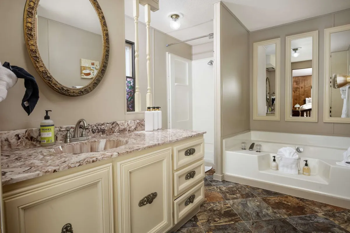 A luxurious bathroom with a marble vanity, large round mirror, and inviting bathtub. The elegant, spa-like setting is designed for ultimate relaxation and self-care routines, echoing the section’s mention of a soaking tub and private bath.