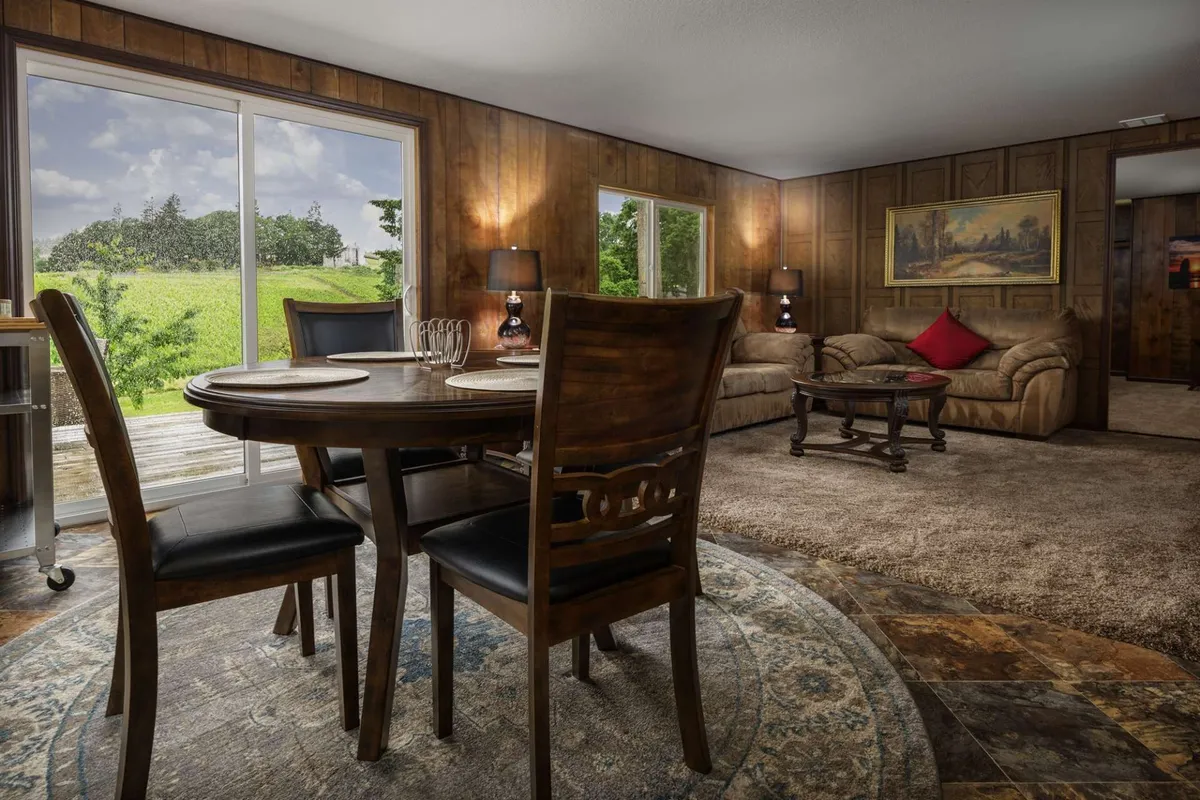 A spacious dining and living area with a large dining table, a comfortable sofa, and expansive windows that let in plenty of daylight. Tasteful artwork and soft furnishings contribute to a warm, inviting atmosphere ideal for shared meals or relaxed conversation.